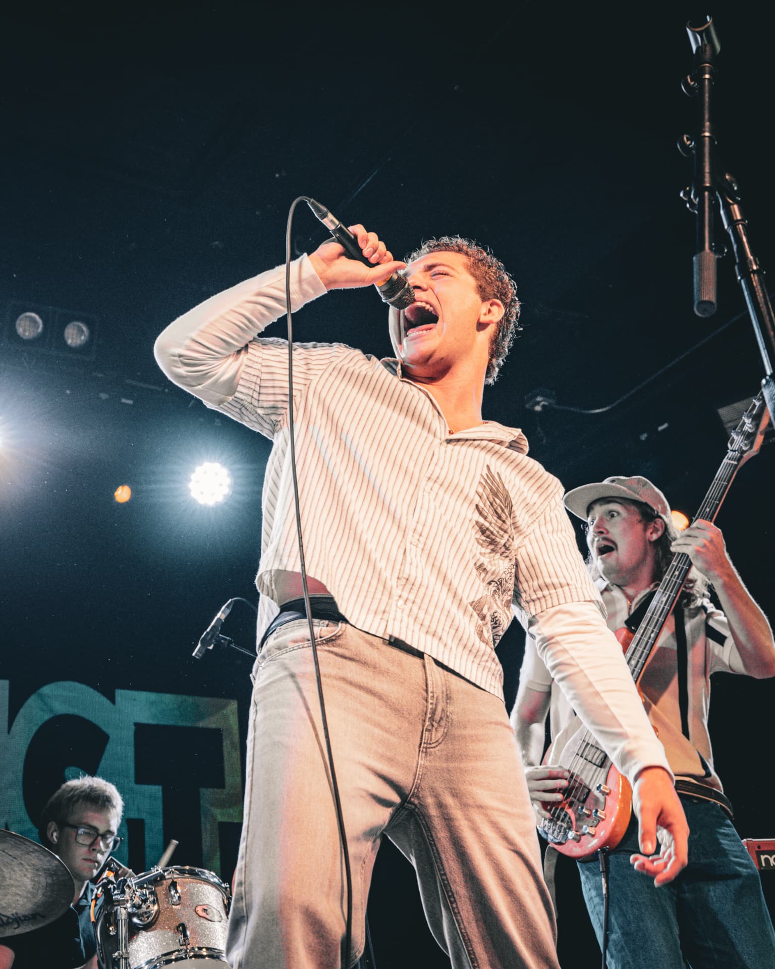 Davey J belting a note on stage with the bassist and drummer behind him