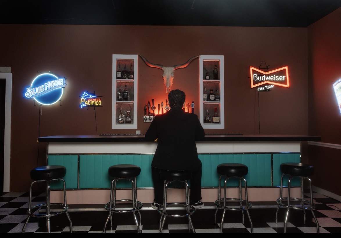 Davey J sitting at a bar surrounded by neon signs